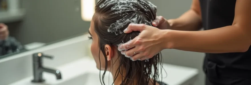 Professionnel coiffeur appliquant un shampoing expert sur cheveux mouillés au-dessus d'un lavabo de salon, mains en mouvement, mousse abondante, texture luxe